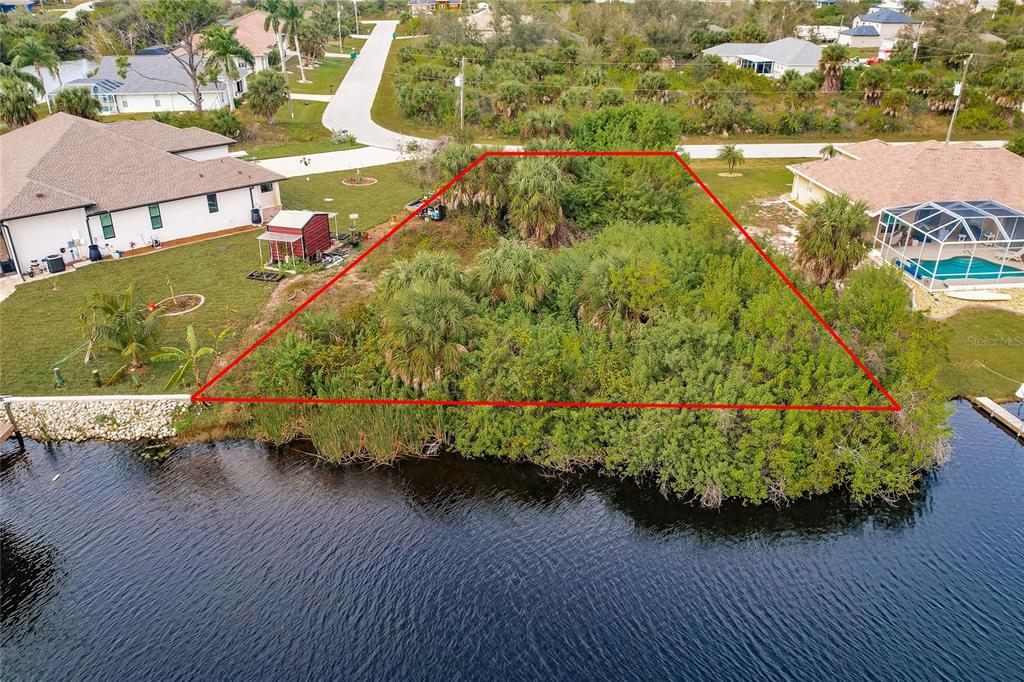 An aerial view shows a vacant, wooded waterfront lot outlined in red between two houses — 9462 WACKER TERRACE, PORT CHARLOTTE, FL