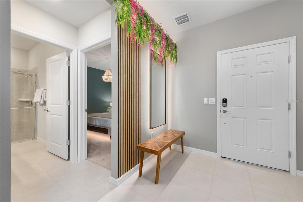 An entryway features a wooden slat wall, a bench, a mirror, and hanging floral decor — 4322 LANA AVENUE, DAVENPORT, FL