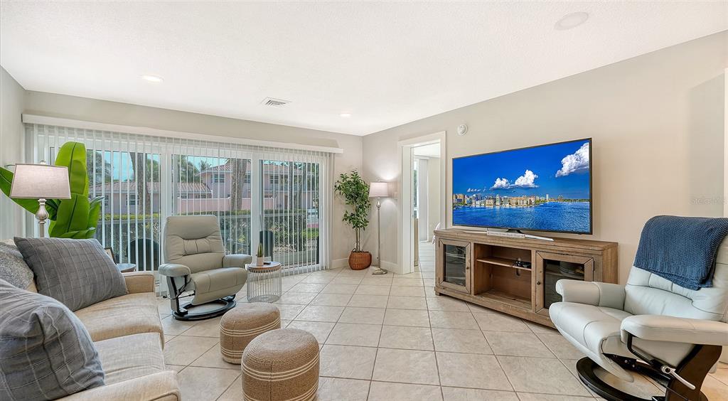 A living room features tile flooring, two light-colored recliners, a sofa, and a large television — 500 S WASHINGTON DRIVE UNIT 6A, SARASOTA, FL