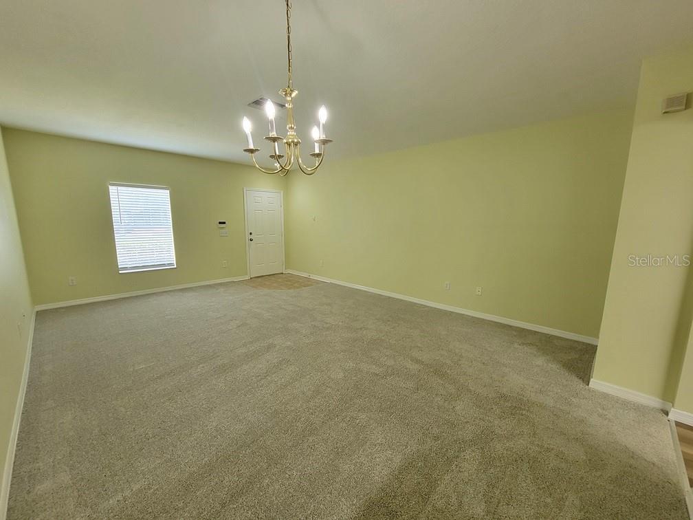 An empty room features beige carpeting, light green walls, and a brass chandelier — 16414 SWAN VIEW CIRCLE UNIT 16414, ODESSA, FL