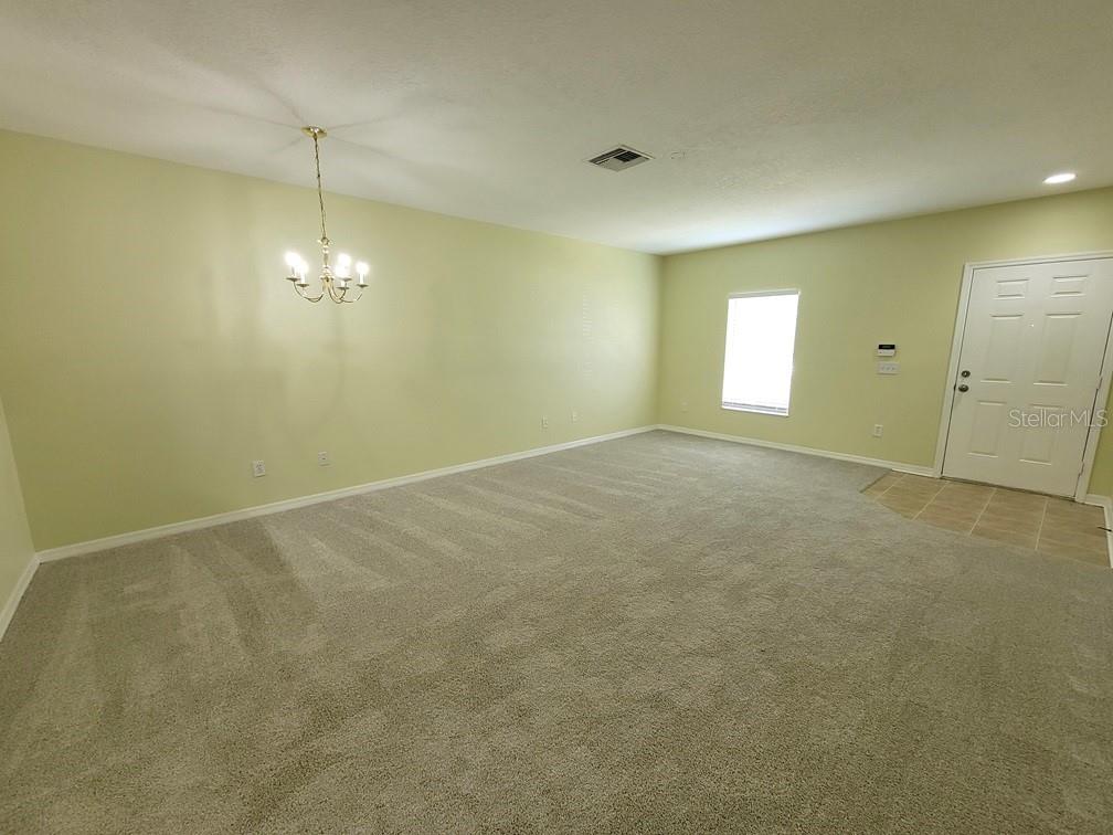 An empty living room features light green walls, beige carpeting, a chandelier, and a front door — 16414 SWAN VIEW CIRCLE UNIT 16414, ODESSA, FL