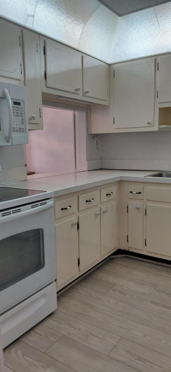 A kitchen features off-white cabinets, white countertops, a white stove, and light wood-look flooring — 2616 Garden Drive N # 303, FL 33461, FL