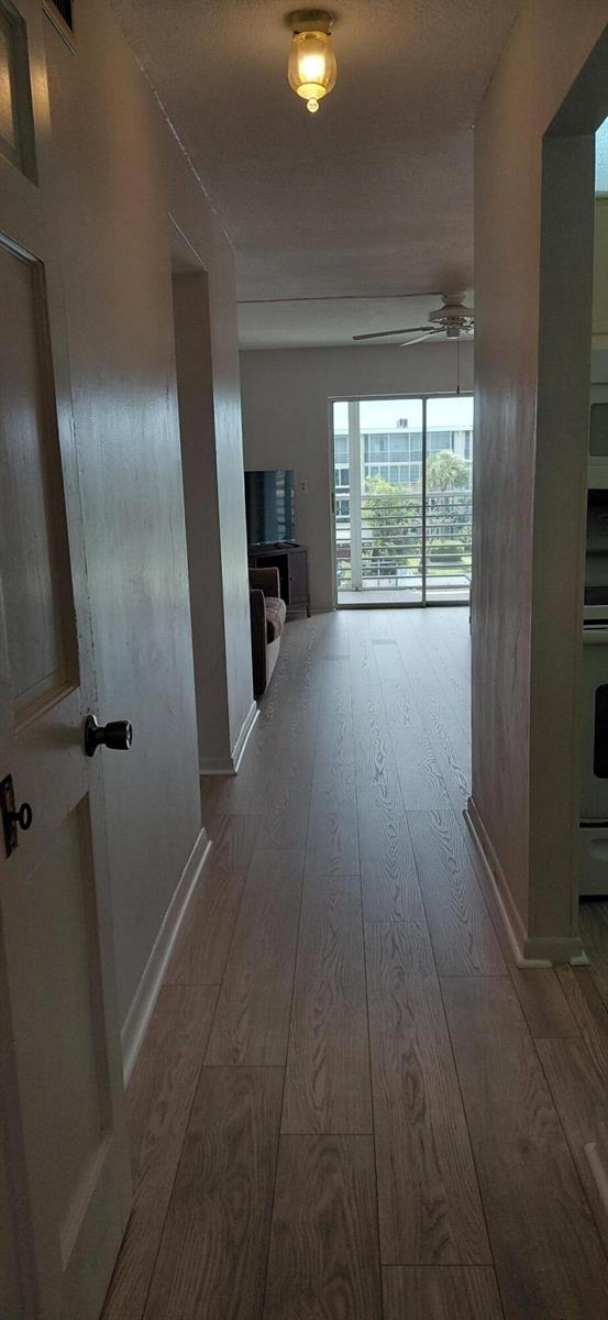 A hallway with light wood-look flooring leads toward a living area with a sliding glass door — 2616 Garden Drive N # 303, FL 33461, FL
