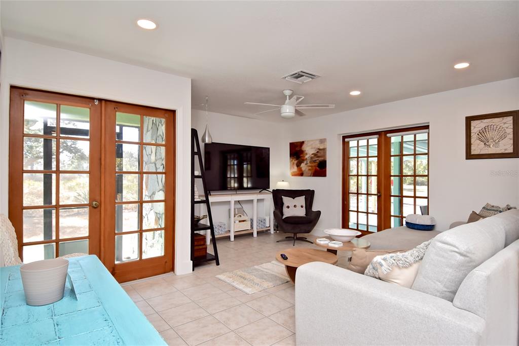 A living room features a white sofa, a television, and two sets of French doors — 7037 DUKE STREET, ENGLEWOOD, FL