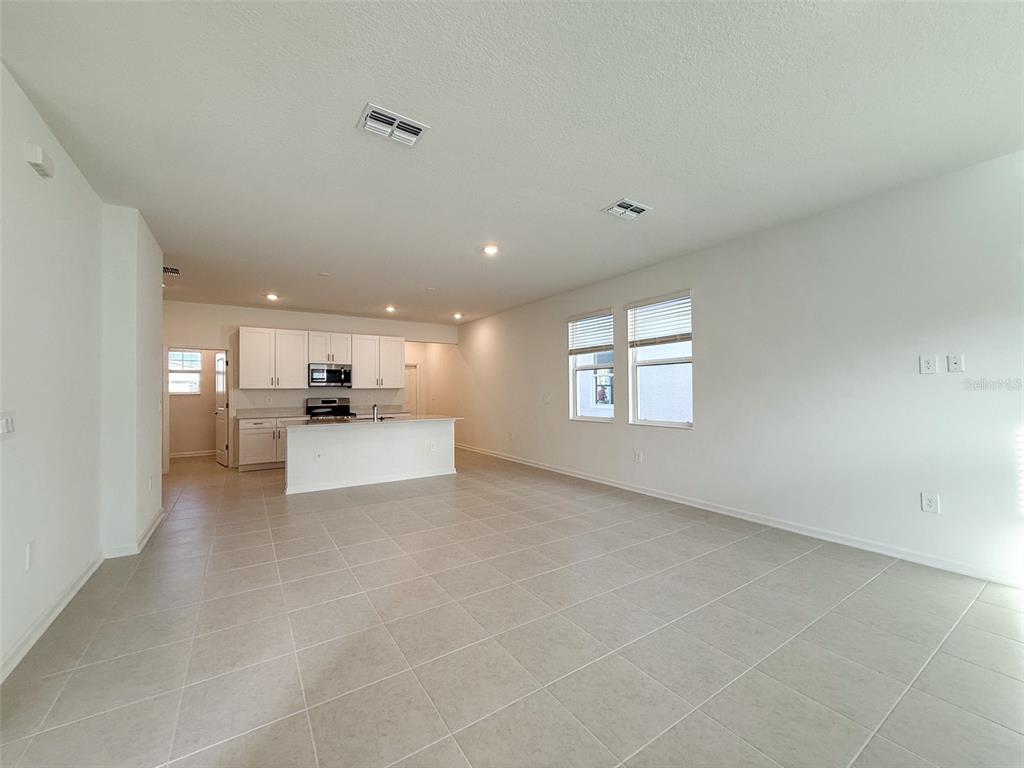 An open-concept kitchen and living area features white cabinetry, tile flooring, and recessed lighting — 1898 RIDER RAIN LANE, APOPKA, FL