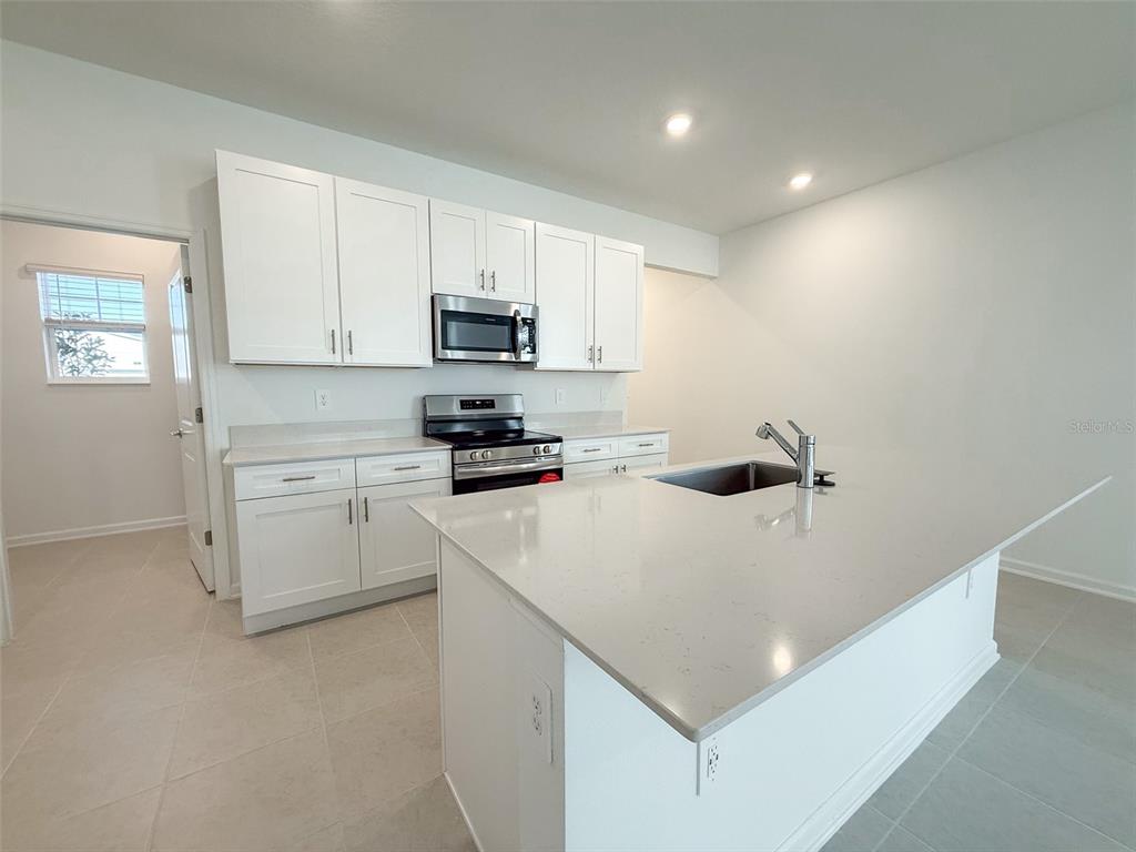 A modern kitchen features white cabinetry, stainless steel appliances, and a large quartz-topped island — 1898 RIDER RAIN LANE, APOPKA, FL