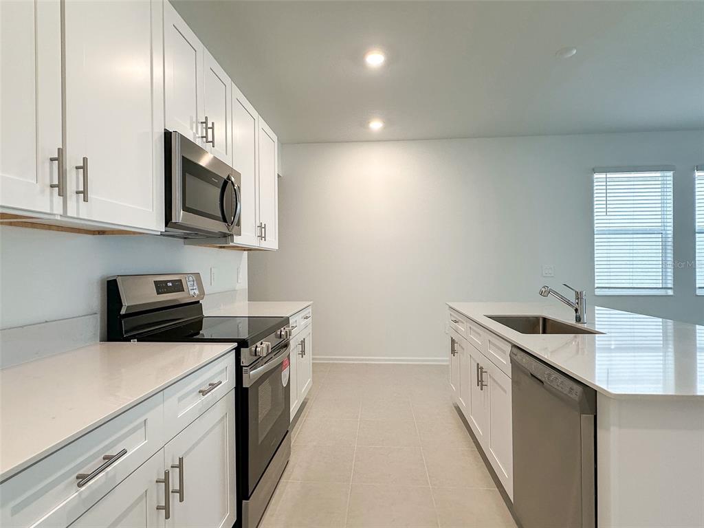 A modern kitchen features white cabinets, stainless steel appliances, and a central island with sink — 1898 RIDER RAIN LANE, APOPKA, FL