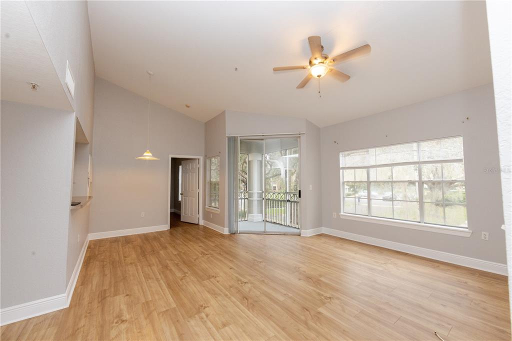 A living room with light wood-look flooring, vaulted ceilings, a ceiling fan, and sliding doors — 2302 MID TOWN TERRACE UNIT 1228, ORLANDO, FL