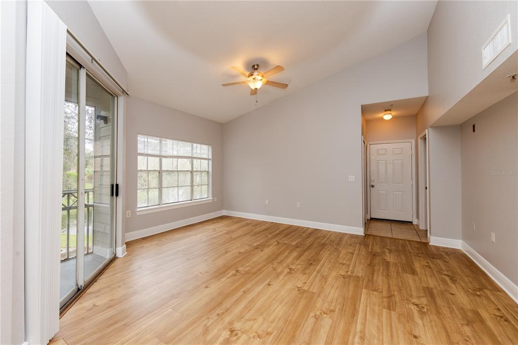An empty living room features wood-look flooring, a vaulted ceiling, a ceiling fan, and windows — 2302 MID TOWN TERRACE UNIT 1228, ORLANDO, FL