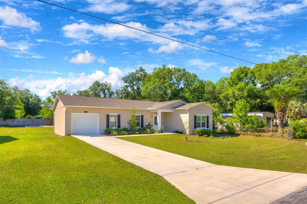 A tan, single-story house with a white garage and a concrete driveway sits on grass — 174 DOVER LN, DELAND, FL