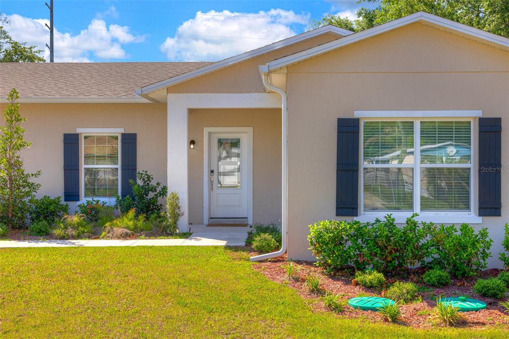 A single-story house exterior features a white front door, dark shutters, and landscaped front yard — 174 DOVER LN, DELAND, FL
