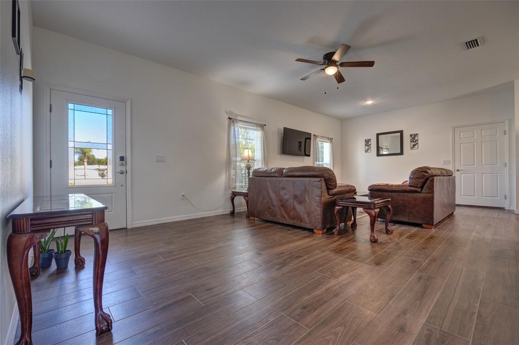 A living room features dark wood-look tile flooring, leather furniture, and a ceiling fan — 174 DOVER LN, DELAND, FL