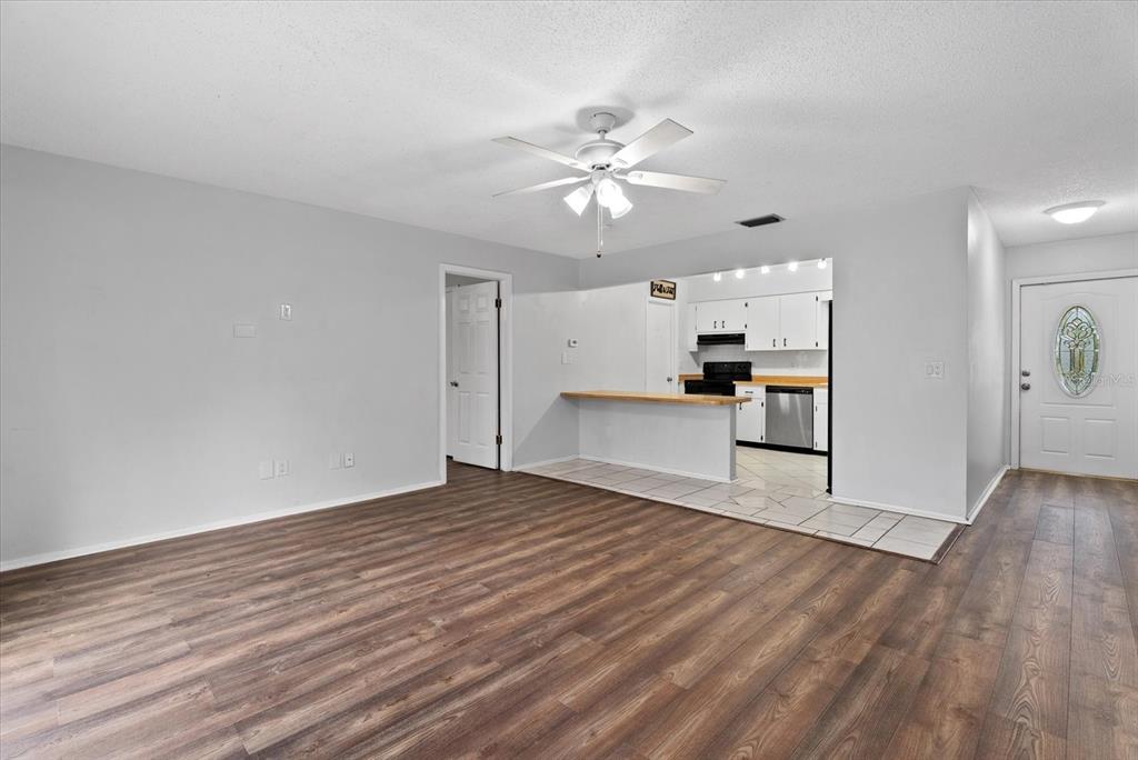A living room with wood-look flooring leads into a kitchen with white cabinets and tile — 519 64TH AVENUE DRIVE E, BRADENTON, FL