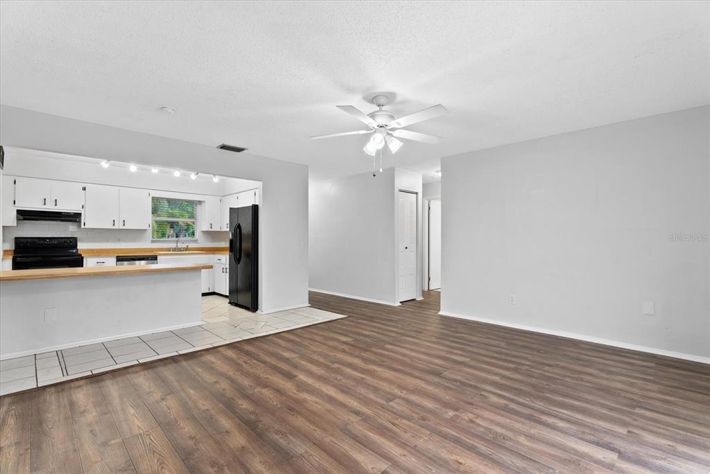 An open-concept living room with wood-look flooring connects to a kitchen with white cabinetry — 519 64TH AVENUE DRIVE E, BRADENTON, FL