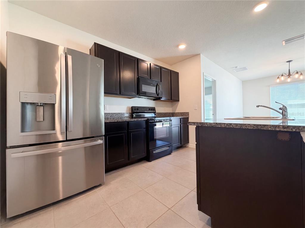 A kitchen features dark wood cabinets, granite countertops, stainless steel appliances, and tile flooring — 11835 MYRTLE ROCK DRIVE, RIVERVIEW, FL