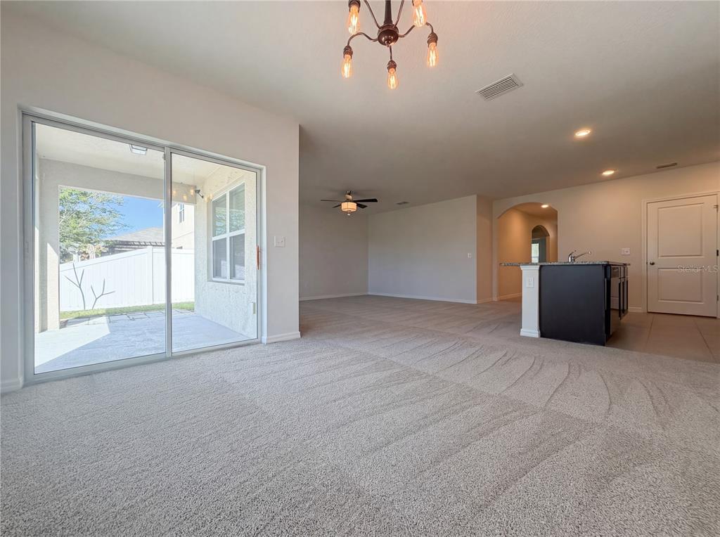 A carpeted living area features a sliding glass door, a kitchen island, and overhead lighting — 11835 MYRTLE ROCK DRIVE, RIVERVIEW, FL