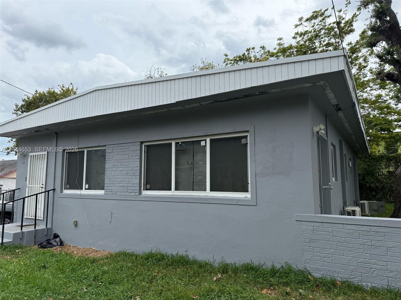 A gray, single-story house exterior features a white roofline, brick accents, and metal security doors — 170 NE 68th Ter, Miami FL 33138, MIAMI, FL