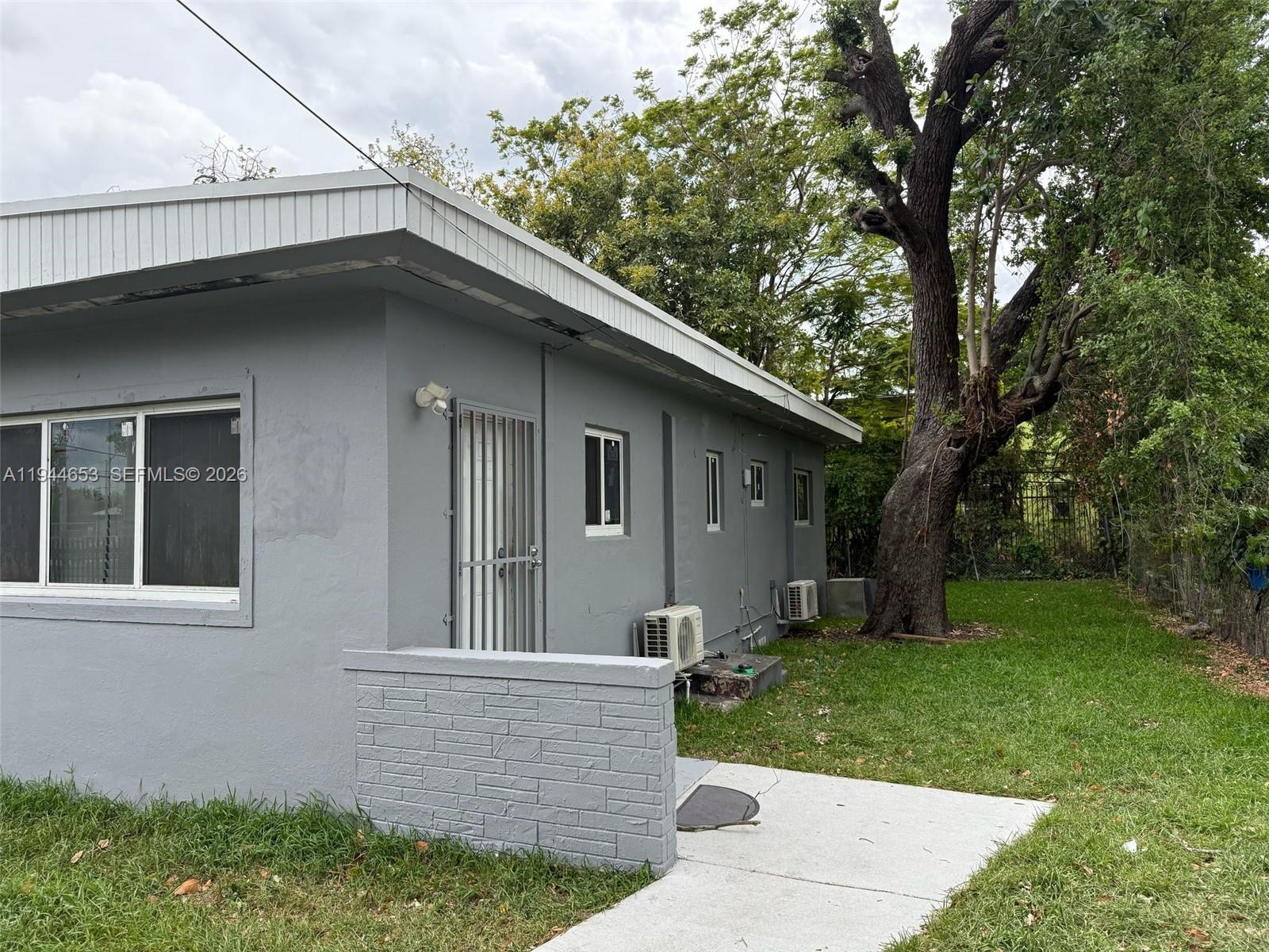 The exterior of a grey, single-story house features a small concrete patio and lawn — 170 NE 68th Ter, Miami FL 33138, MIAMI, FL