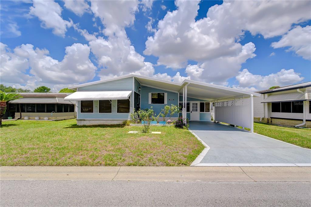 A light blue single-story manufactured home with a carport and a front lawn — 35123 COLONY HILLS DRIVE, ZEPHYRHILLS, FL