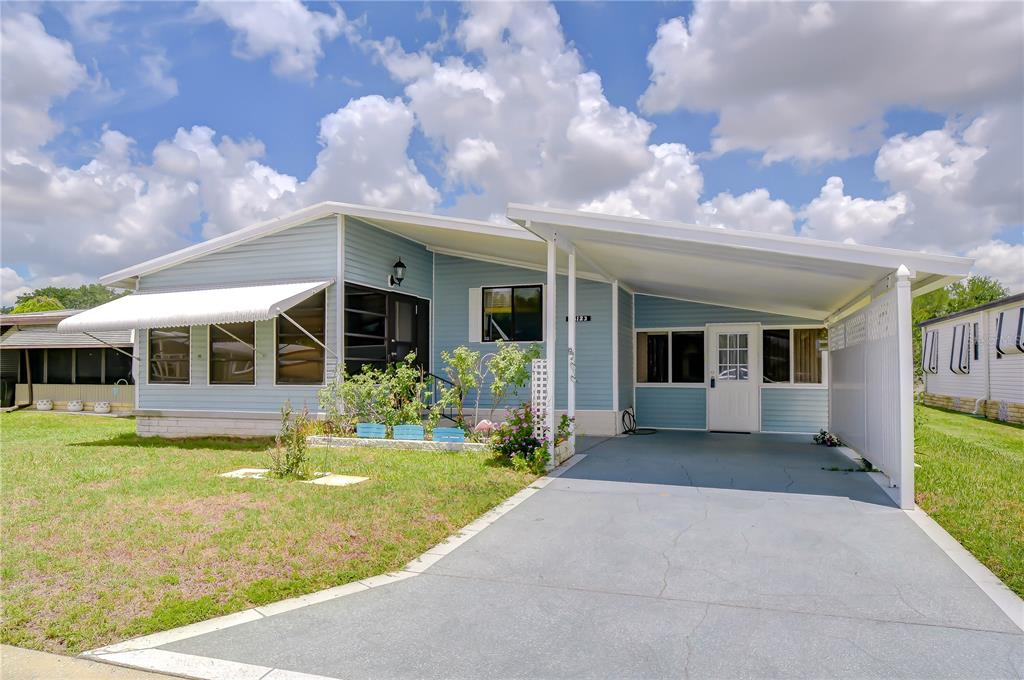 A light blue manufactured home features a front carport, a screened porch, and a lawn — 35123 COLONY HILLS DRIVE, ZEPHYRHILLS, FL