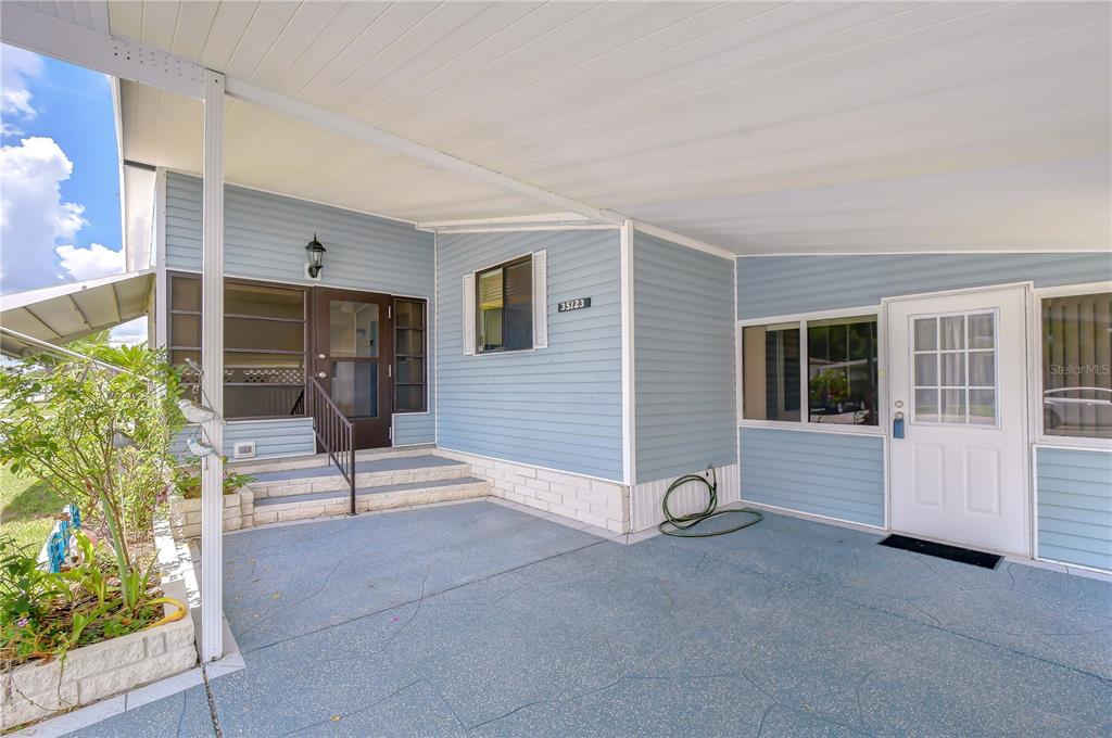 A light blue mobile home exterior features a covered concrete carport and a front entrance — 35123 COLONY HILLS DRIVE, ZEPHYRHILLS, FL