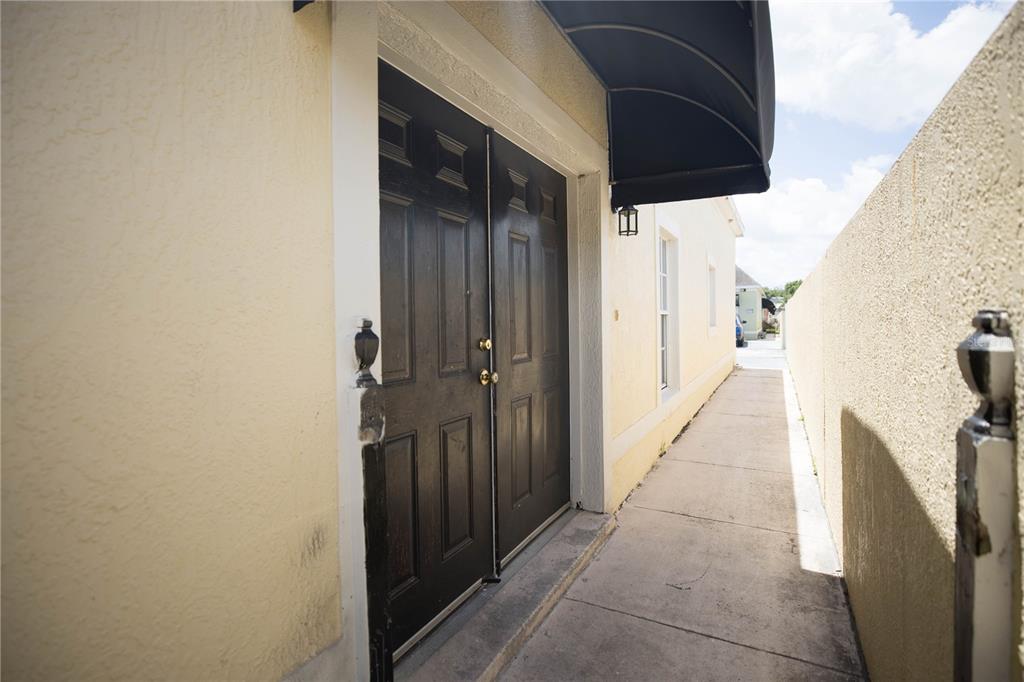 A narrow concrete walkway leads to a set of black double doors with an awning — 1055 UNIVERSAL REST PLACE, KISSIMMEE, FL