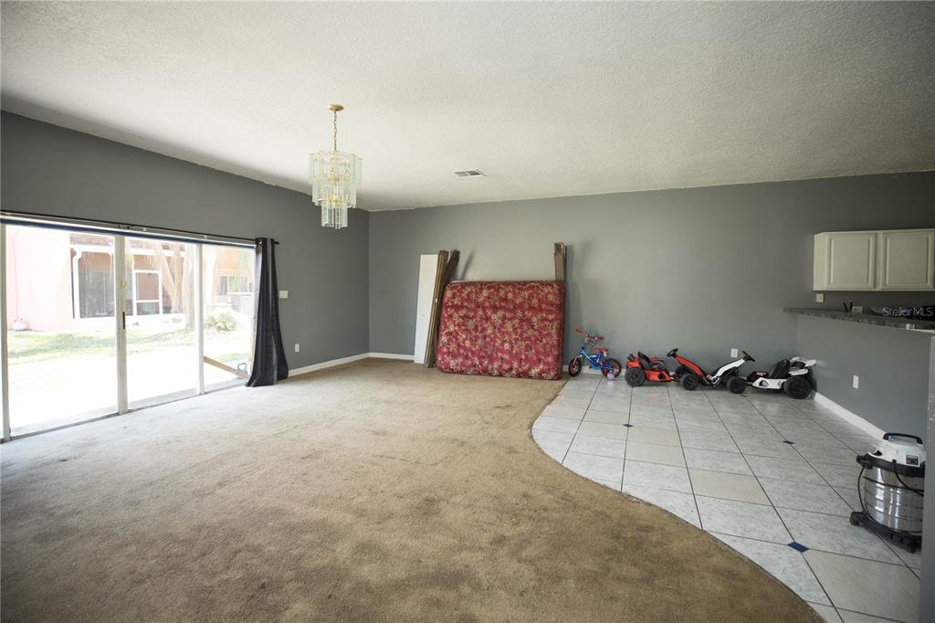 A living room features a mix of carpet and tile flooring, a chandelier, and sliding doors — 1055 UNIVERSAL REST PLACE, KISSIMMEE, FL
