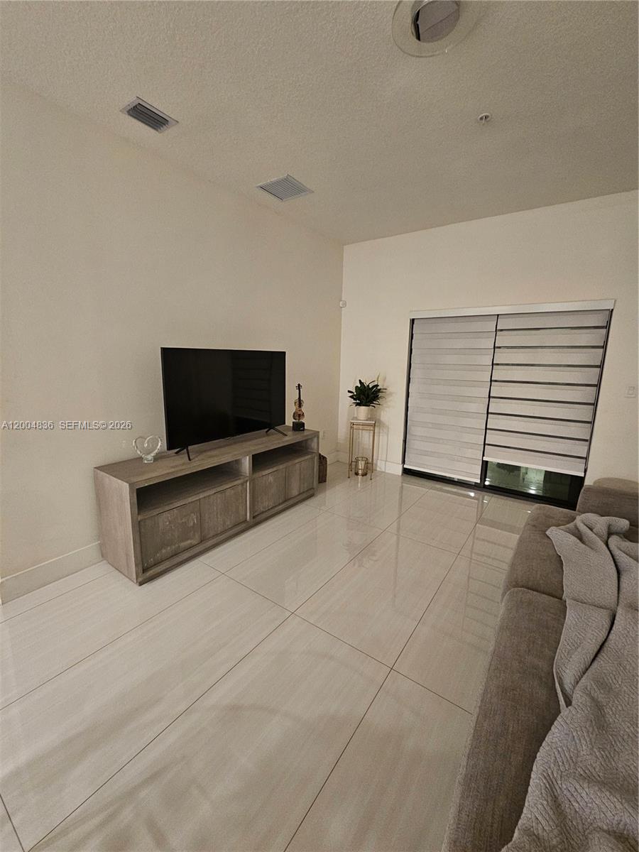 A living room features a television on a wooden console, tile flooring, and sliding doors — 8167 NW 41st St # 109, Doral FL 33166, DORAL, FL