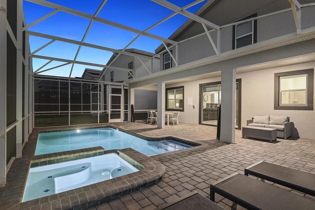A screened-in patio features a swimming pool, a hot tub, and outdoor seating at dusk — 9012 SOMMERSET HILLS DRIVE, DAVENPORT, FL