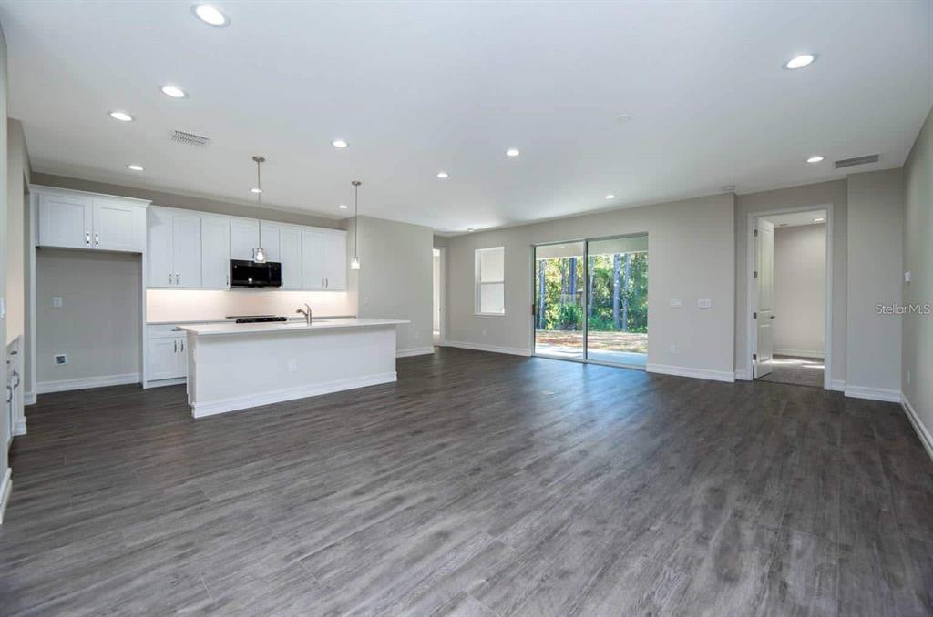 A modern open-concept kitchen and living area featuring white cabinetry, an island, and wood-look flooring — 8340 NW 17TH CIRCLE, OCALA, FL
