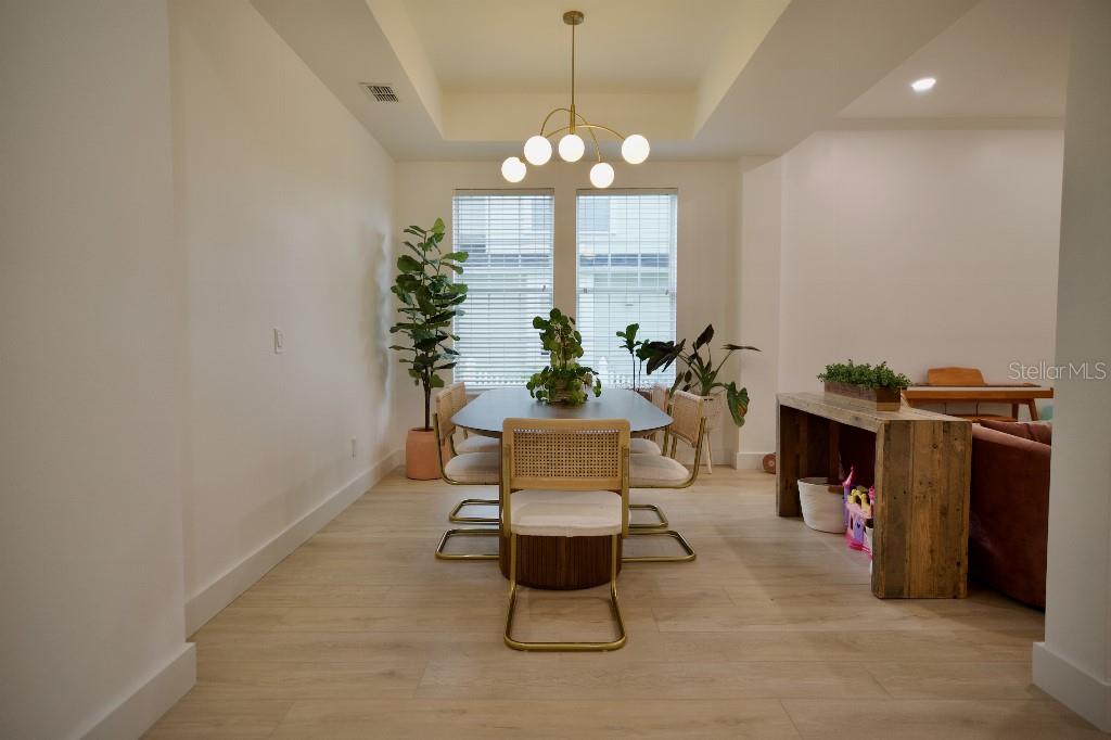 A dining room features a modern chandelier, a wooden table with cane chairs, and light flooring — 311 REEVES STREET, KISSIMMEE, FL