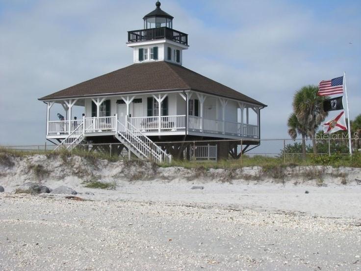 A white lighthouse-style building stands on stilts above a sandy beach with three flags flying — 13180 AMARYLLIS CIRCLE, PORT CHARLOTTE, FL