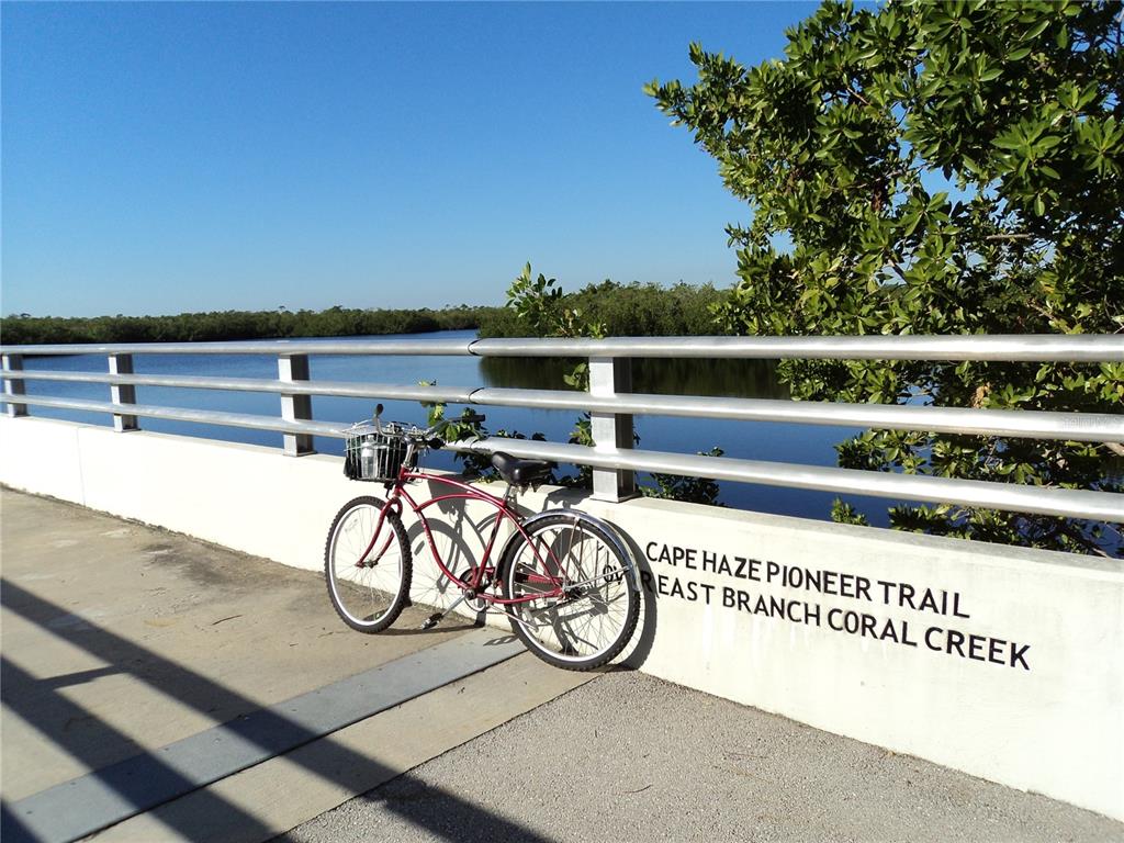 A red bicycle leans against a bridge railing overlooking a waterway on a sunny day — 13180 AMARYLLIS CIRCLE, PORT CHARLOTTE, FL