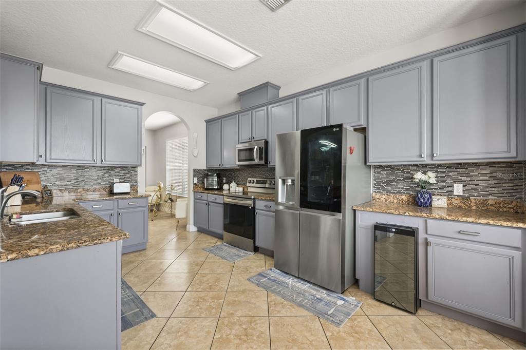 A kitchen features gray cabinets, granite countertops, stainless steel appliances, and light-colored tile flooring — 12657 IRIS LAKE DRIVE, ORLANDO, FL
