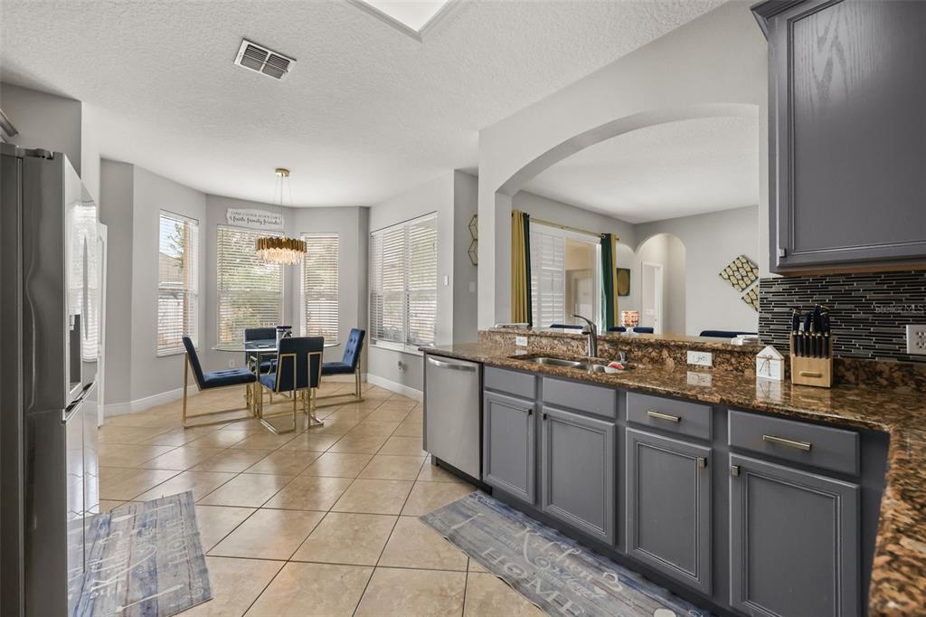 A kitchen with gray cabinets and granite countertops opens to a dining area with tile floors — 12657 IRIS LAKE DRIVE, ORLANDO, FL