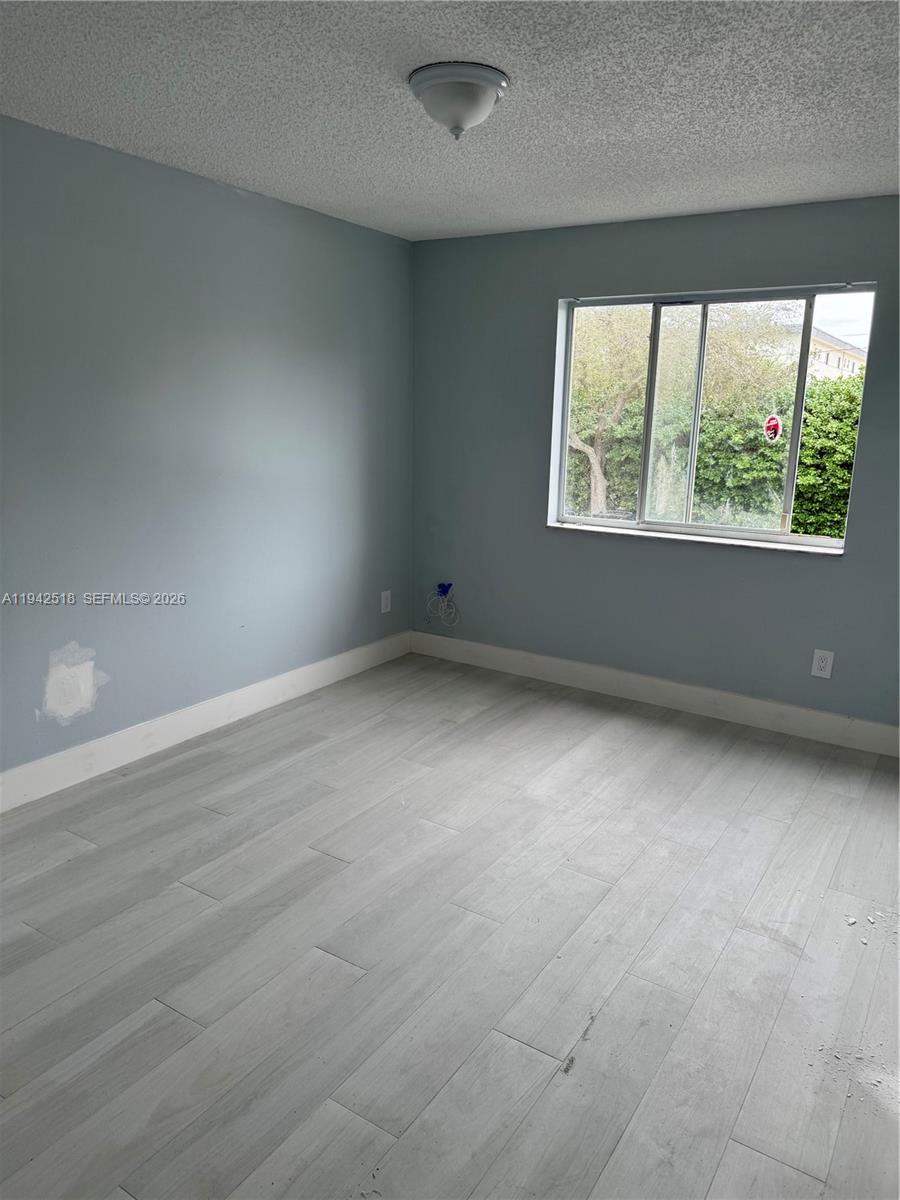 An empty bedroom features light blue walls, wood-look tile flooring, and a single window — 440 S Park Rd # 207, Hollywood FL 33021, HOLLYWOOD, FL