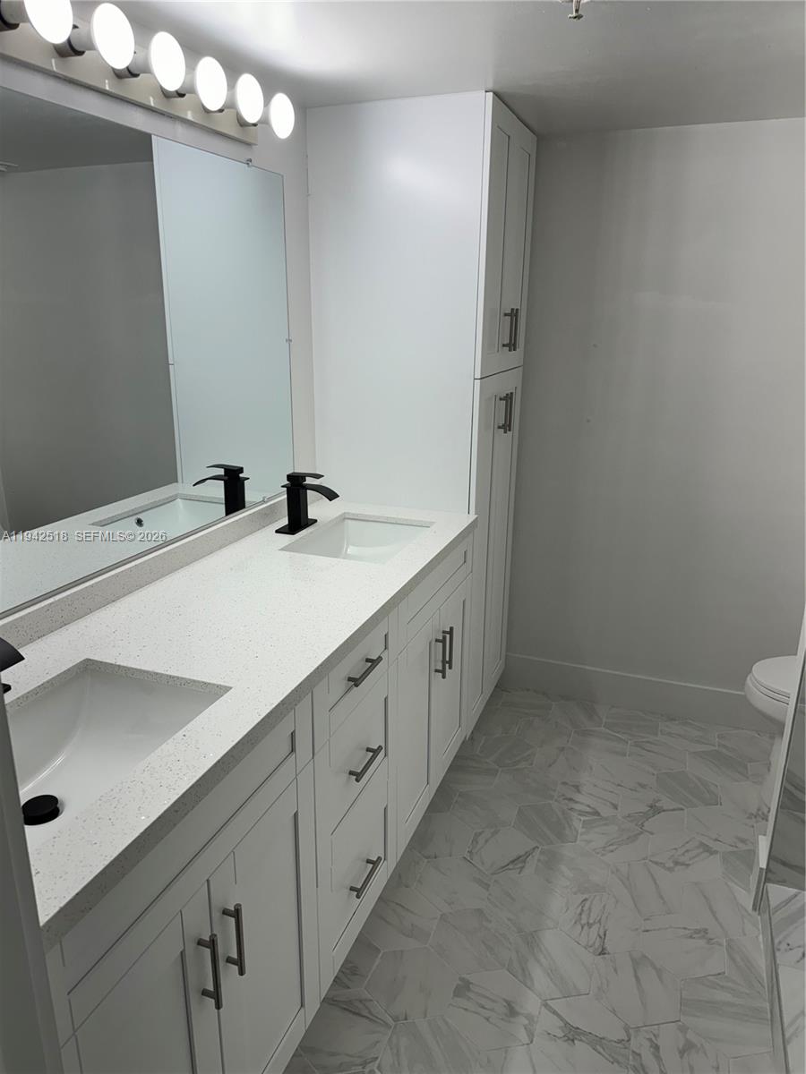 A modern bathroom features a double vanity with white cabinets, quartz countertops, and black fixtures — 440 S Park Rd # 207, Hollywood FL 33021, HOLLYWOOD, FL
