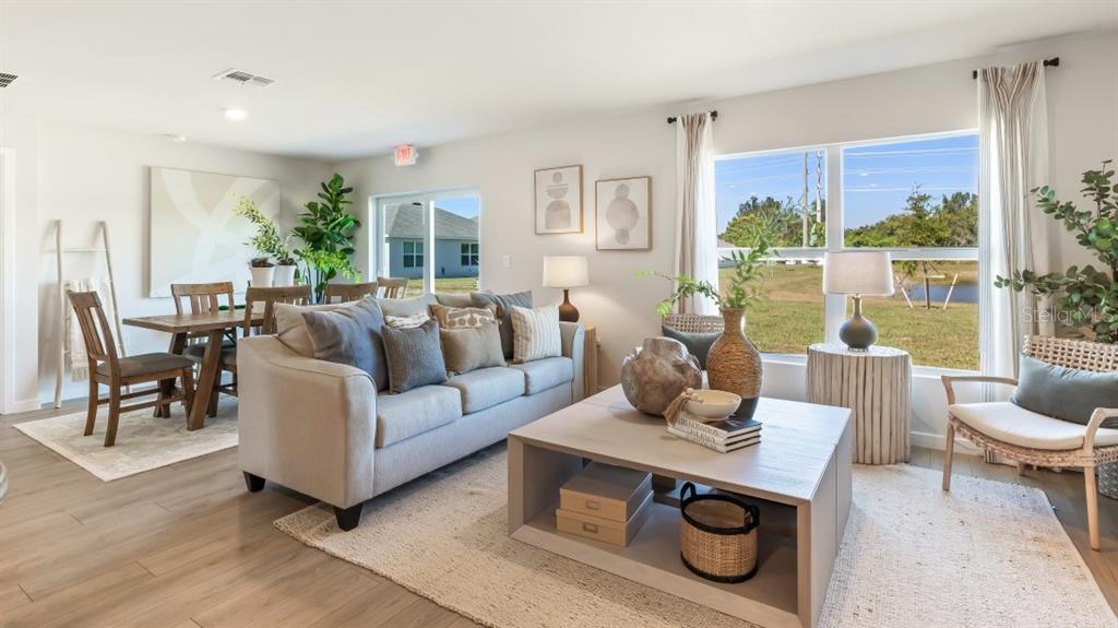 A bright living and dining area features light wood flooring, neutral furniture, and large windows — 1557 POWELL VALLEY DRIVE, PORT CHARLOTTE, FL