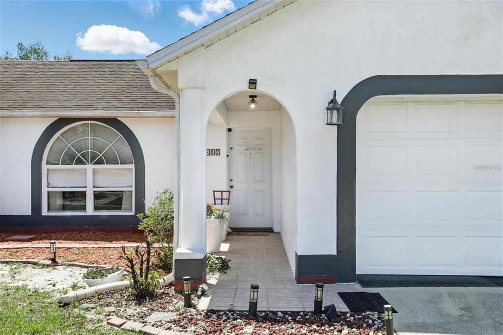 The exterior of a white house features an arched entryway, a garage, and a window — 417 JEFFERS STREET, DELTONA, FL