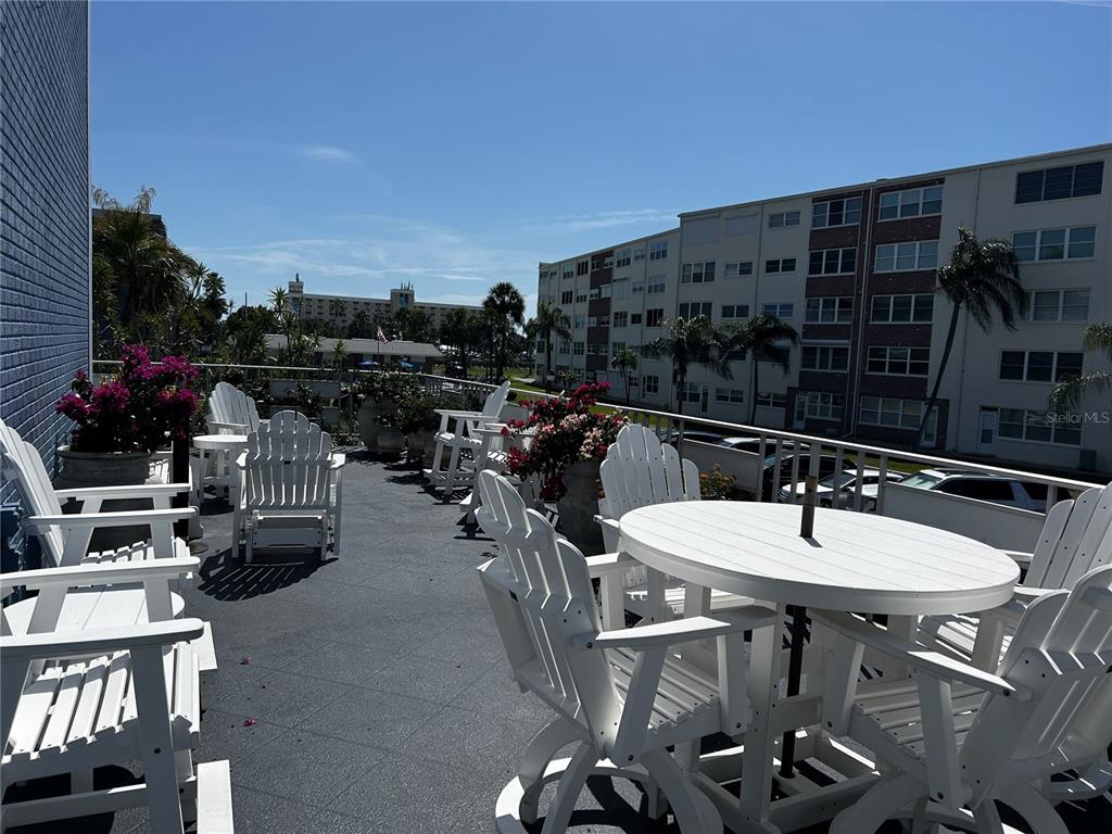 An outdoor balcony features white patio furniture, potted flowers, and views of nearby apartment buildings — 5555 GULF BOULEVARD UNIT 310, ST PETE BEACH, FL