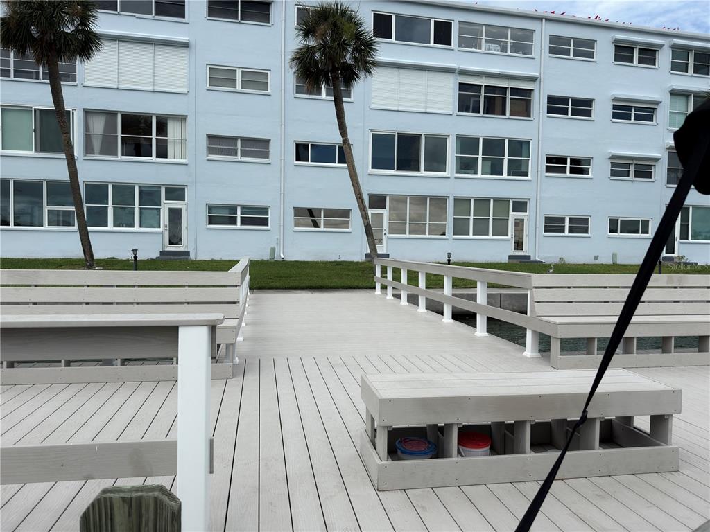 A wooden deck with built-in benches overlooks a multi-story light blue apartment building — 5555 GULF BOULEVARD UNIT 310, ST PETE BEACH, FL