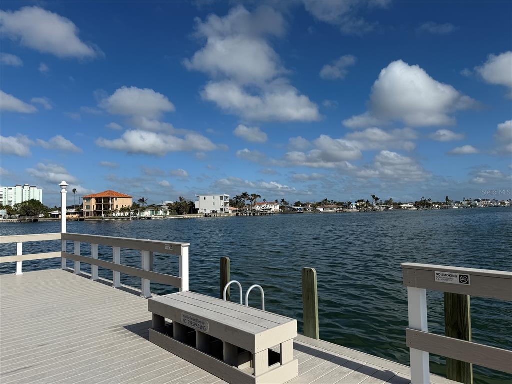 A wooden pier overlooks a calm bay with houses along the distant shoreline — 5555 GULF BOULEVARD UNIT 310, ST PETE BEACH, FL