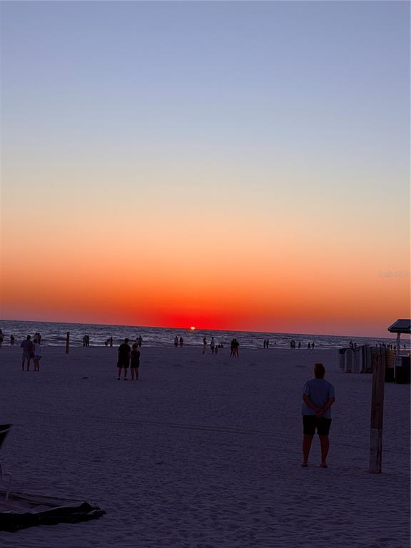 A sunset view over a sandy beach with several people standing near the water — 5555 GULF BOULEVARD UNIT 310, ST PETE BEACH, FL