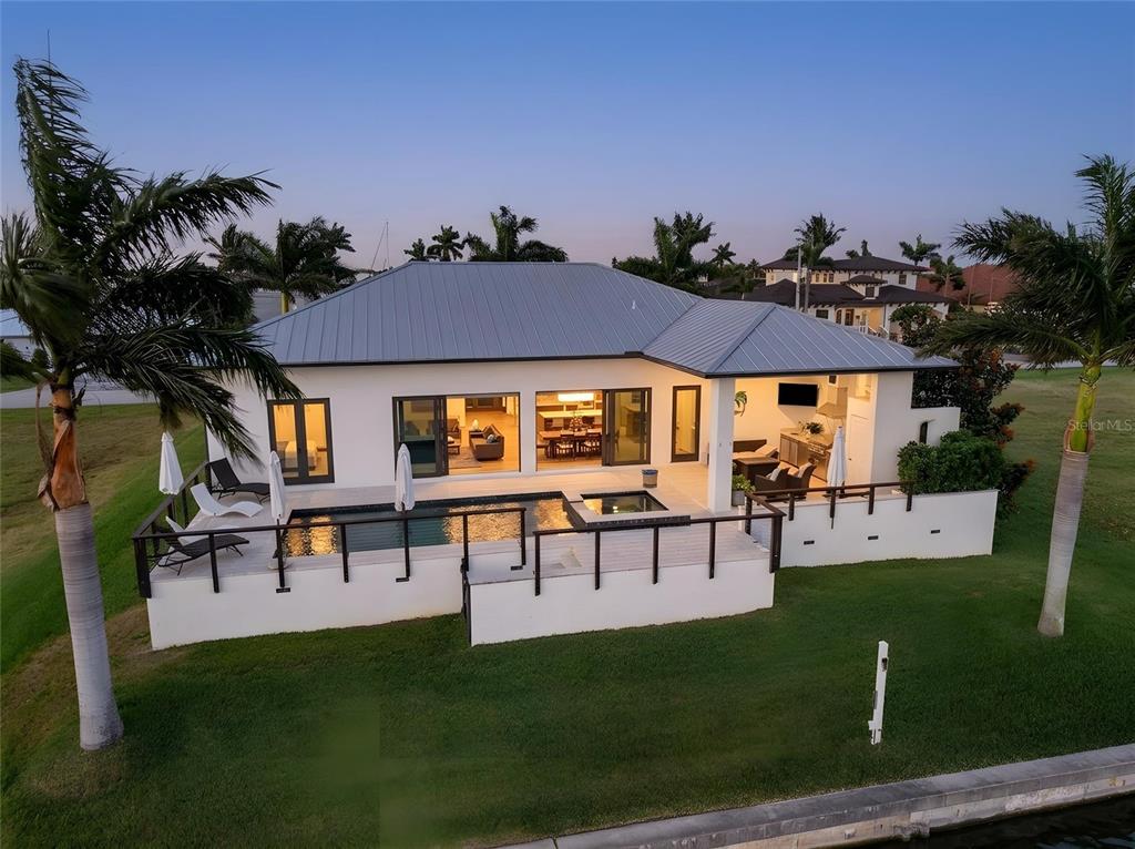 An aerial view of a white house with a metal roof, pool, and waterfront lawn — 125 COLONY POINT DRIVE, PUNTA GORDA, FL