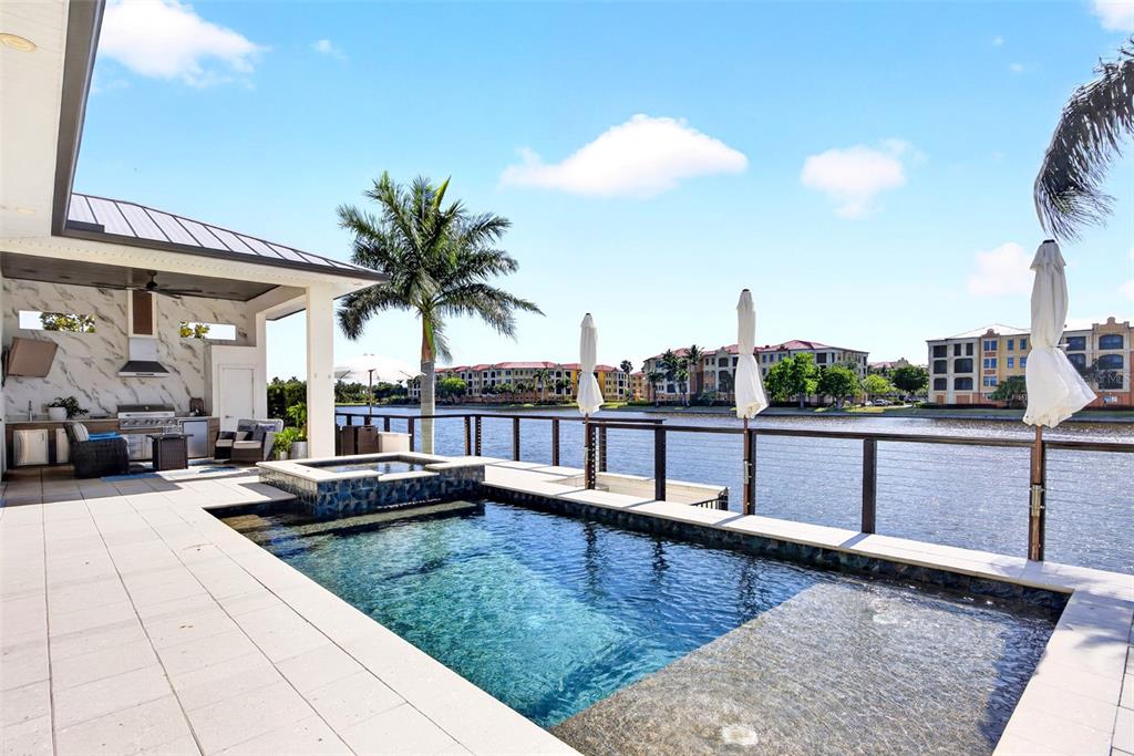 A patio features a pool, a hot tub, and an outdoor kitchen overlooking a lake — 125 COLONY POINT DRIVE, PUNTA GORDA, FL