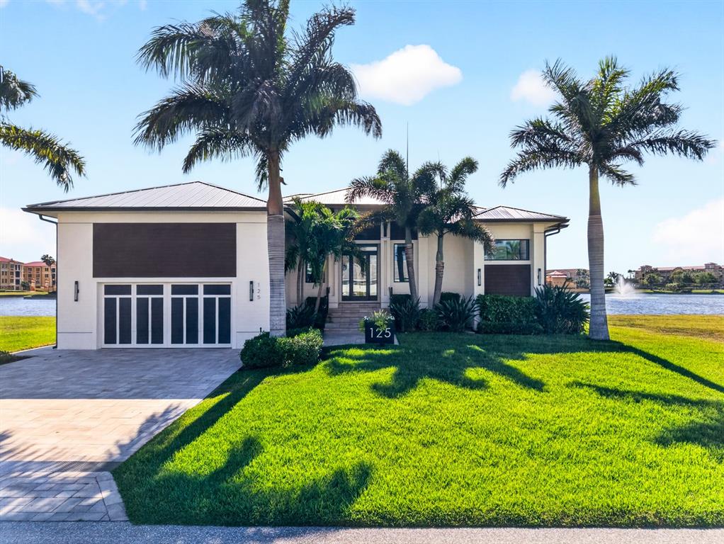 A single-story house with a white exterior, a multi-car garage, and palm trees sits lakeside — 125 COLONY POINT DRIVE, PUNTA GORDA, FL