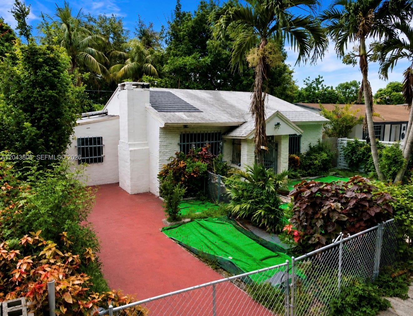 A white, single-story house features a red driveway, a chimney, and a chain-link fence — 7573 NW 12th Ct, Miami FL 33147, MIAMI, FL