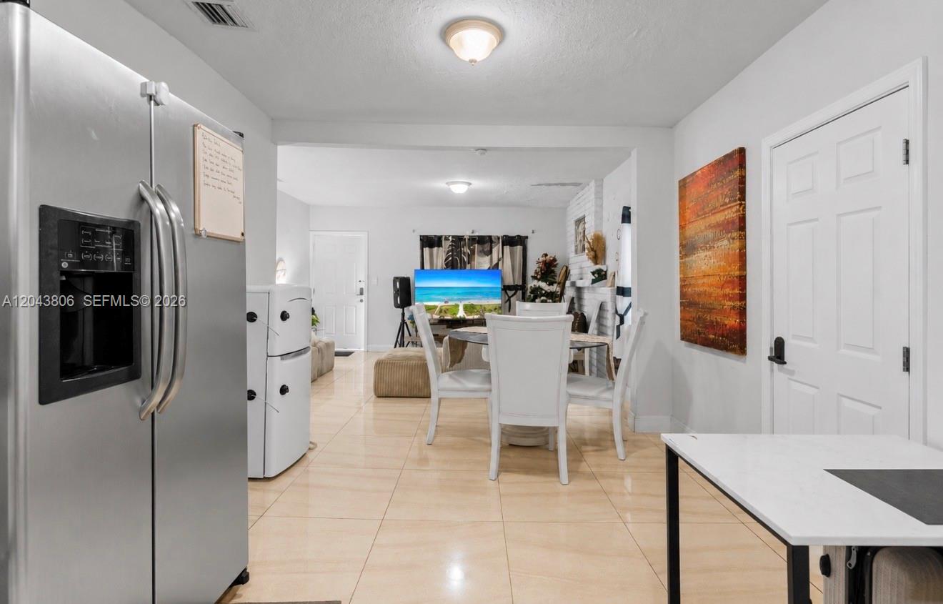 A dining area with a glass table and white chairs sits between a kitchen and living room — 7573 NW 12th Ct, Miami FL 33147, MIAMI, FL