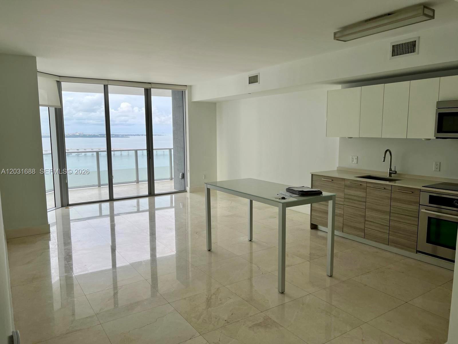 A modern kitchen with light wood cabinets and a dining table overlooks a water view — 1300 Brickell Bay Dr # 3506, Miami FL 33131, MIAMI, FL