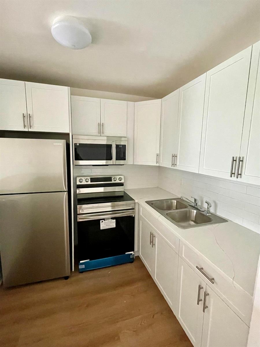 A kitchen features white cabinets, stainless steel appliances, a double sink, and light wood flooring — 203 Easthampton I, West Palm Beach FL 33417, WEST PALM BEACH, FL